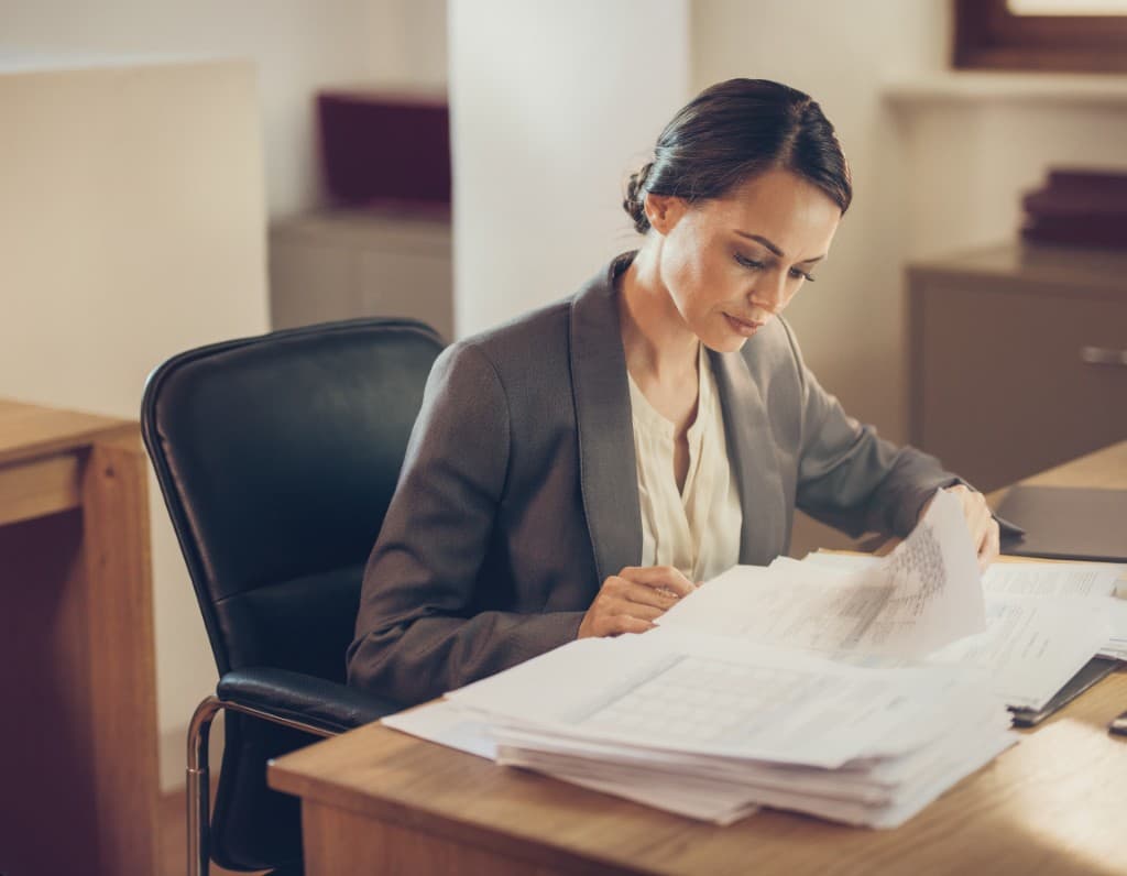 Claims professional at a wooden desk reviewing a thick stack of claim file paperwork
